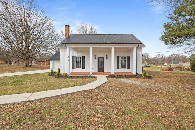 view of front of house with a garage, concrete driveway, a chimney, covered porch, and a front yard