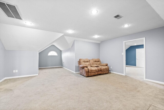 living area featuring light colored carpet, visible vents, vaulted ceiling, and baseboards