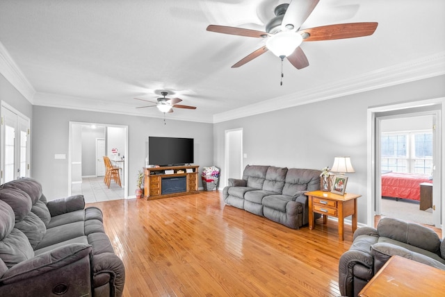 living room featuring crown molding, light wood-style floors, a ceiling fan, and a healthy amount of sunlight