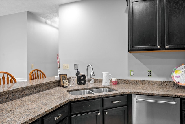 kitchen with dark cabinets, a sink, dishwasher, and light stone countertops