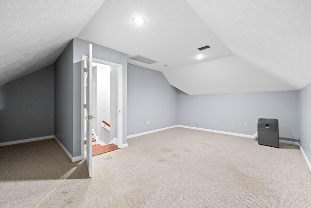 additional living space with a textured ceiling, light colored carpet, visible vents, and baseboards