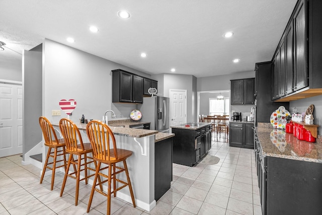 kitchen with stone countertops, a breakfast bar area, a center island, and stainless steel fridge with ice dispenser