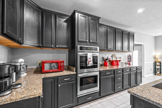 kitchen with dark cabinets, double oven, a textured ceiling, and light tile patterned floors