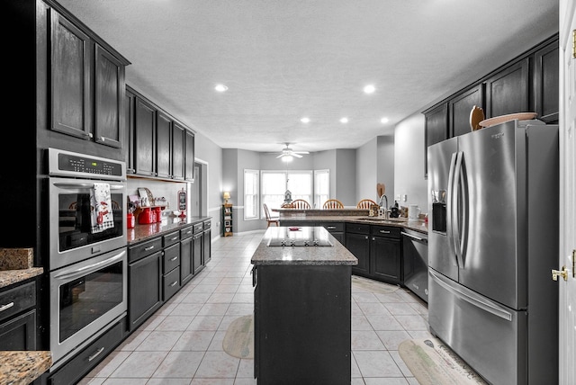 kitchen with light tile patterned floors, appliances with stainless steel finishes, a kitchen island, and light stone countertops