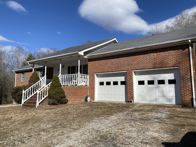 ranch-style home featuring a garage, dirt driveway, roof with shingles, covered porch, and brick siding