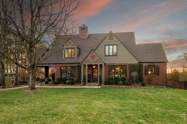 view of front facade with a chimney, a lawn, and brick siding