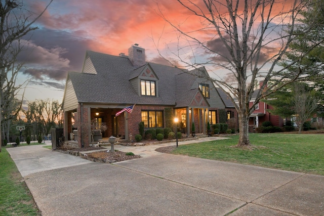 view of front of property with brick siding, a shingled roof, concrete driveway, a chimney, and a front yard