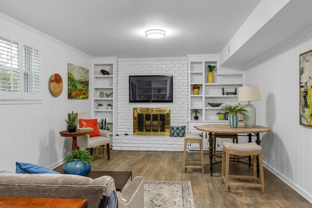 living room featuring visible vents, built in features, wood finished floors, crown molding, and a brick fireplace