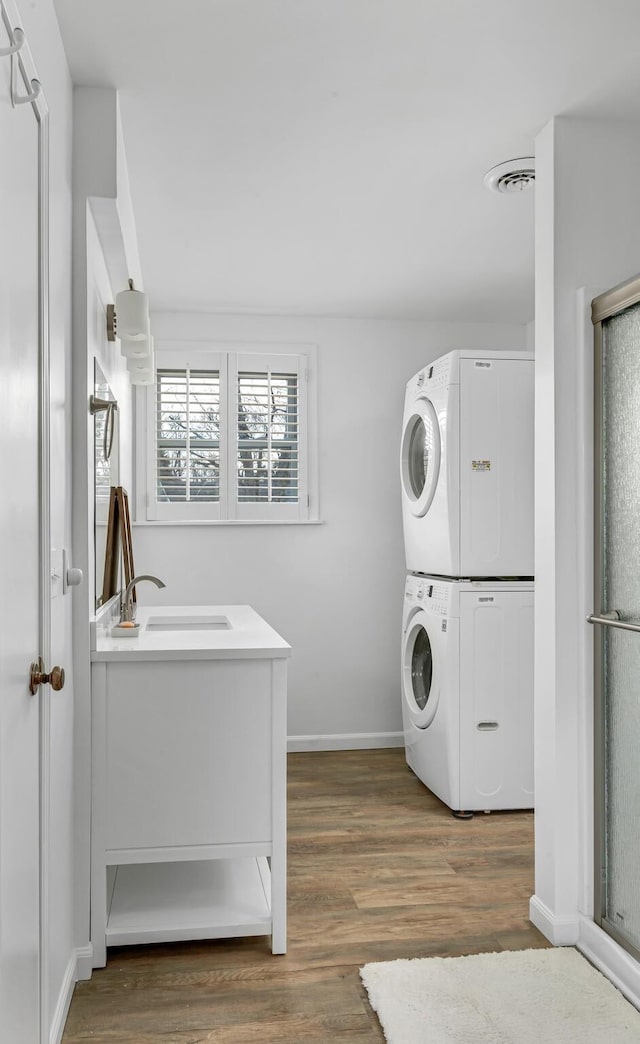 laundry area featuring laundry area, visible vents, dark wood-style flooring, stacked washer / drying machine, and a sink