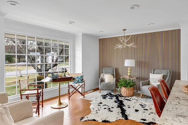 living area with baseboards, crown molding, a chandelier, and wood finished floors