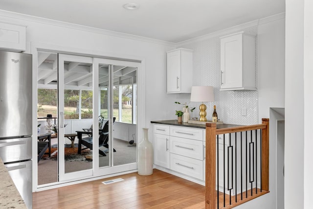 bar with crown molding, tasteful backsplash, visible vents, freestanding refrigerator, and light wood-type flooring