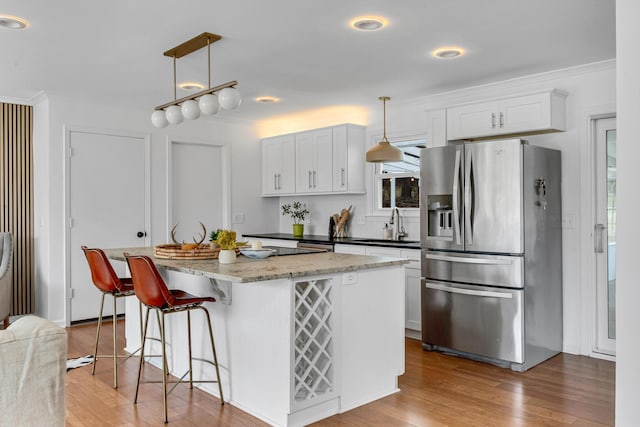 kitchen with decorative light fixtures, white cabinetry, and stainless steel refrigerator with ice dispenser