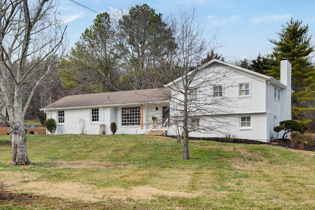 tri-level home with brick siding, a chimney, and a front lawn