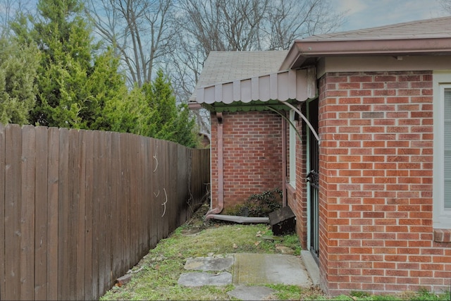 view of side of home with a shingled roof, fence, and brick siding