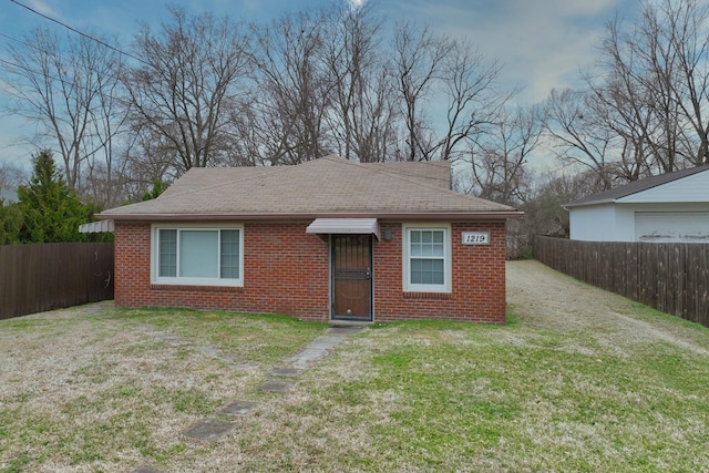 exterior space with brick siding, a fenced backyard, a front lawn, and roof with shingles