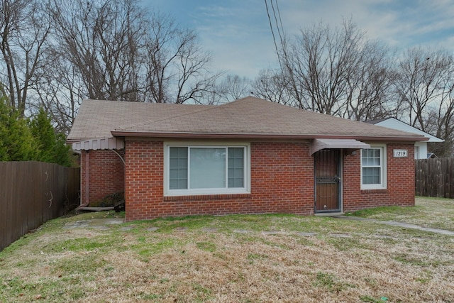 view of front of property featuring a shingled roof, fence, a front lawn, and brick siding