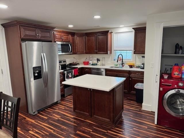 kitchen with appliances with stainless steel finishes, washer / clothes dryer, a center island, light countertops, and a sink