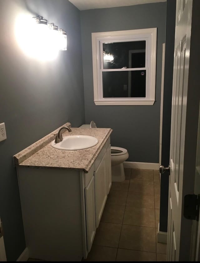 half bath with toilet, tile patterned flooring, baseboards, and vanity