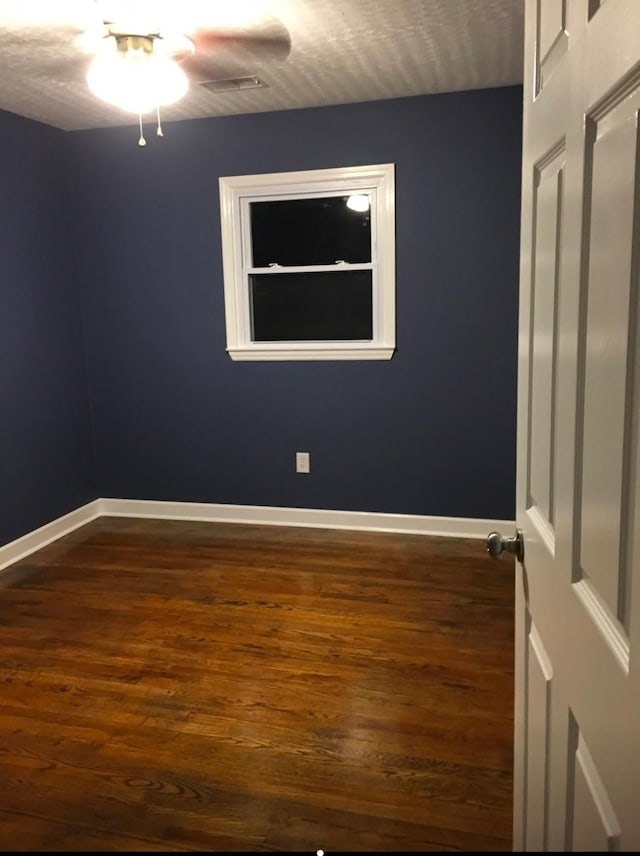 spare room featuring visible vents, baseboards, and dark wood-style flooring