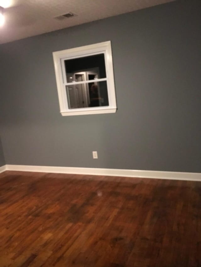 empty room with baseboards, visible vents, and wood finished floors