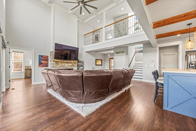 living area featuring ceiling fan, dark wood-type flooring, baseboards, stairs, and beam ceiling