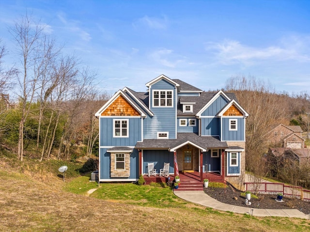 view of front of property with board and batten siding, covered porch, roof with shingles, and a front lawn