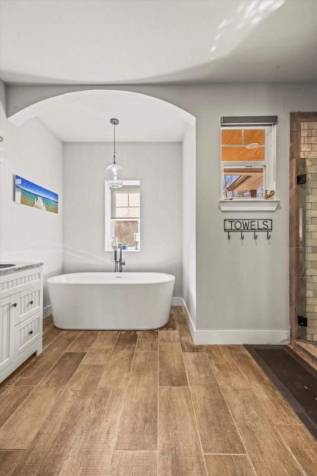 full bathroom with a tile shower, vanity, wood finished floors, a freestanding tub, and baseboards