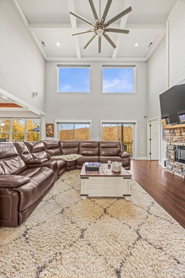 living area featuring a towering ceiling, a stone fireplace, wood finished floors, coffered ceiling, and beamed ceiling