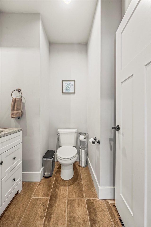 half bath featuring baseboards, vanity, toilet, and wood finished floors