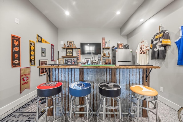 bar featuring freestanding refrigerator, indoor wet bar, baseboards, and recessed lighting