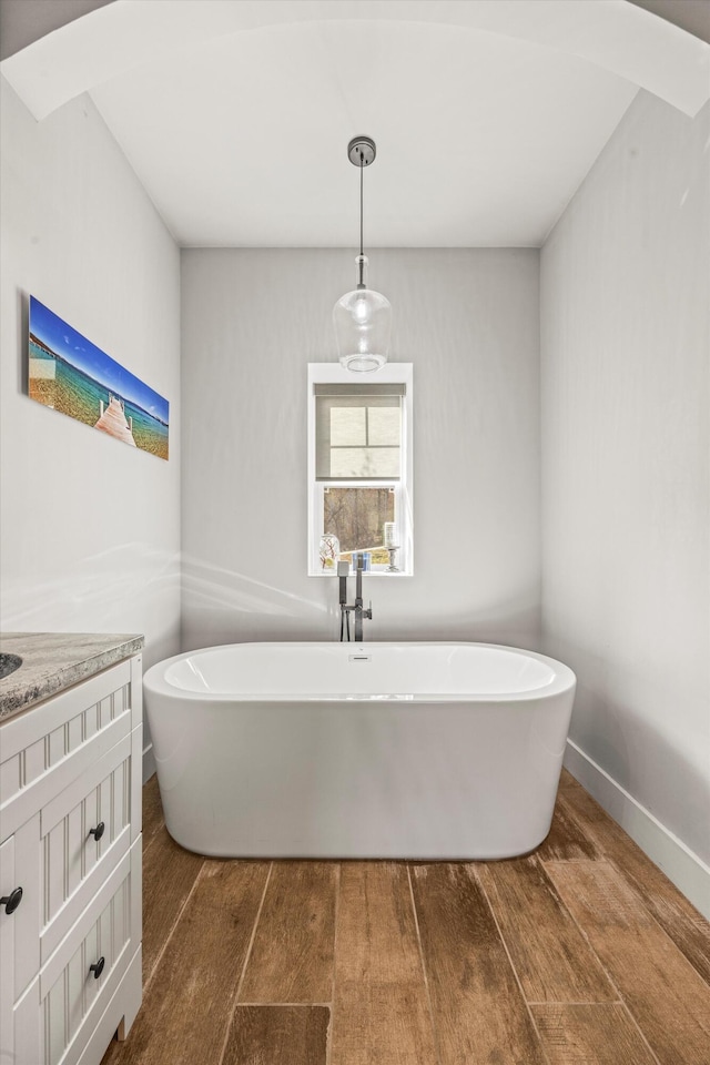 bathroom featuring wood finished floors, a freestanding tub, vanity, and baseboards