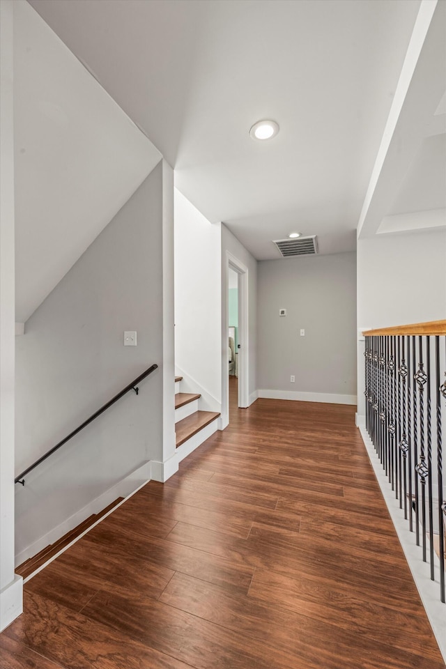 hallway featuring stairs, dark wood-style flooring, visible vents, and baseboards