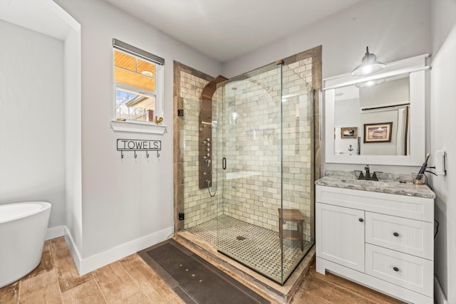 bathroom with baseboards, wood finished floors, vanity, a freestanding tub, and a shower stall