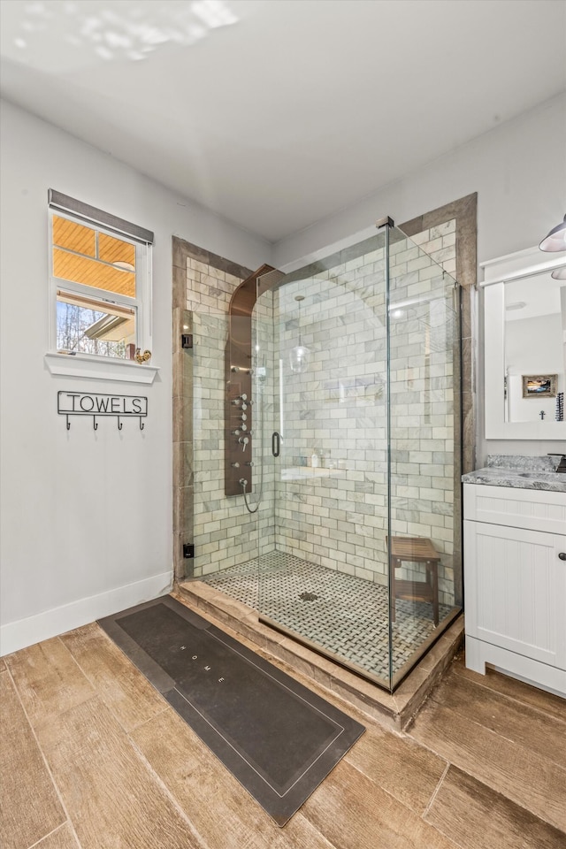 bathroom with wood finished floors, a shower stall, baseboards, and vanity