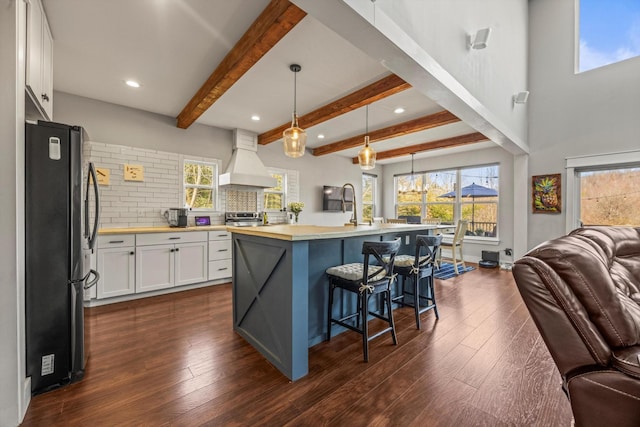 kitchen featuring pendant lighting, a center island with sink, stainless steel appliances, white cabinetry, and premium range hood