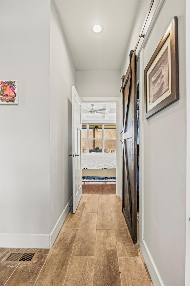 corridor featuring a barn door, light wood-style flooring, and baseboards