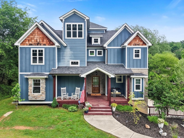 view of front facade with a front lawn, board and batten siding, roof with shingles, and covered porch