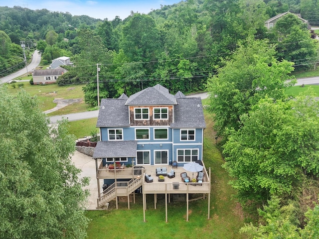 rear view of property with roof with shingles, a deck, and a forest view