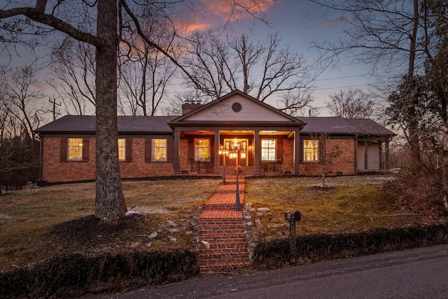 view of front of property with brick siding, a chimney, covered porch, an attached garage, and a front yard