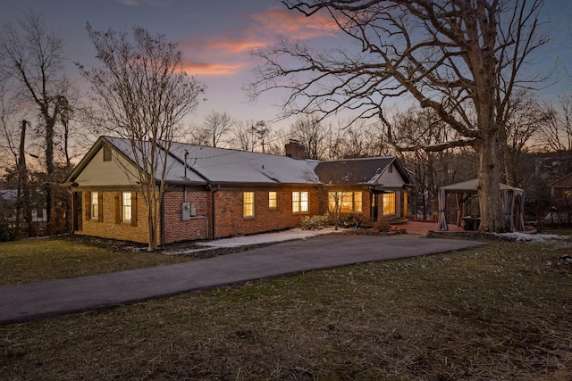 rear view of property featuring brick siding, driveway, a gazebo, a yard, and a chimney