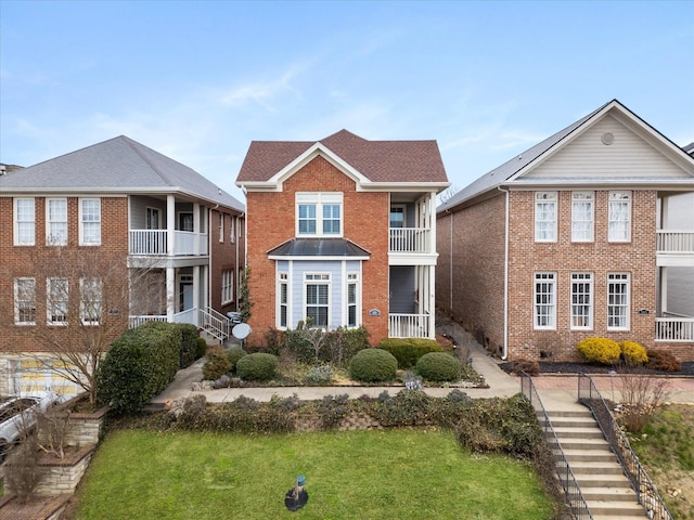 view of front of home featuring a balcony, a front yard, stairway, and brick siding