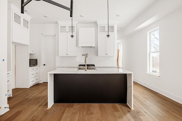 kitchen featuring light stone counters, glass insert cabinets, white cabinetry, hanging light fixtures, and a center island with sink