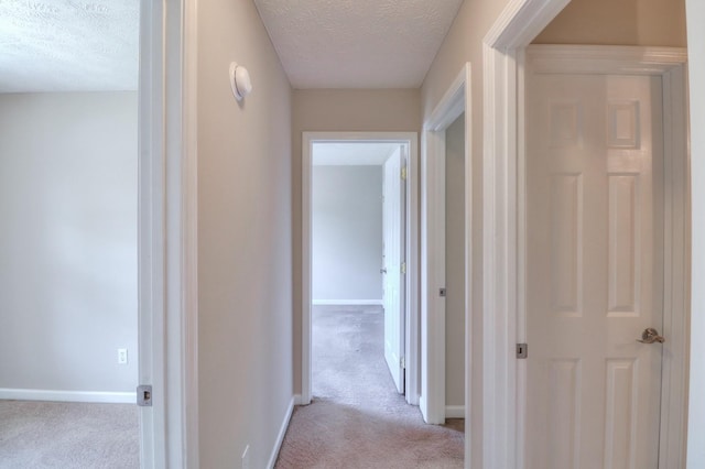 hallway featuring light carpet, baseboards, and a textured ceiling