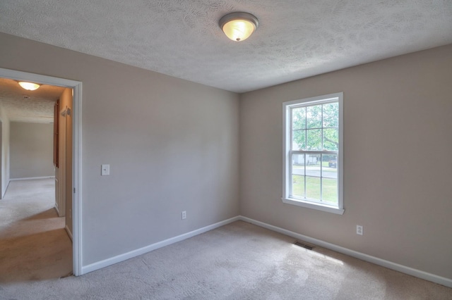 empty room featuring visible vents, light carpet, a textured ceiling, and baseboards