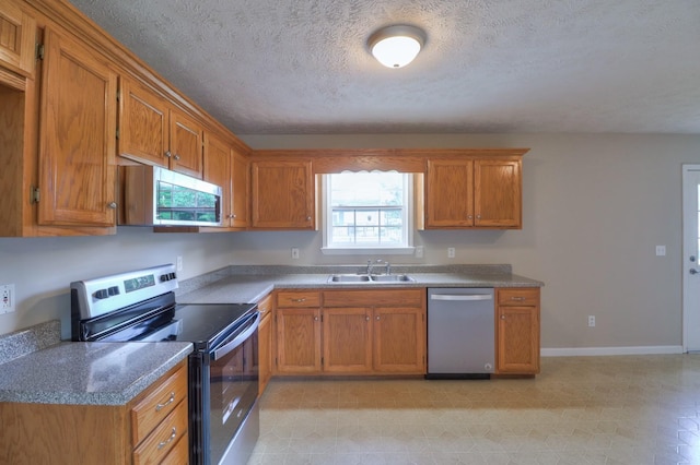 kitchen featuring a textured ceiling, stainless steel appliances, a sink, baseboards, and brown cabinetry