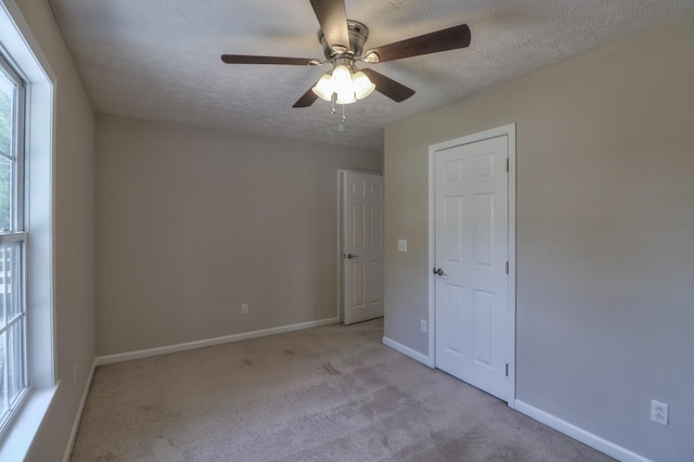 spare room featuring light carpet, ceiling fan, baseboards, and a textured ceiling