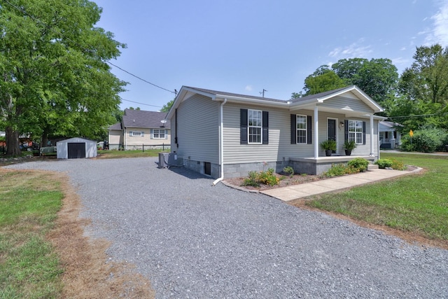 view of front of property with an outbuilding, covered porch, crawl space, a storage unit, and gravel driveway