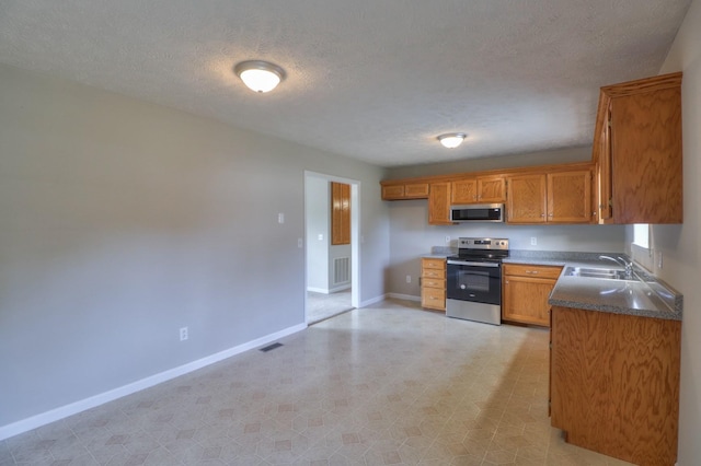 kitchen with brown cabinets, stainless steel appliances, dark countertops, a sink, and baseboards
