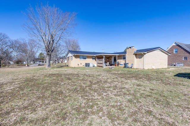 rear view of property with cooling unit, a yard, and a chimney