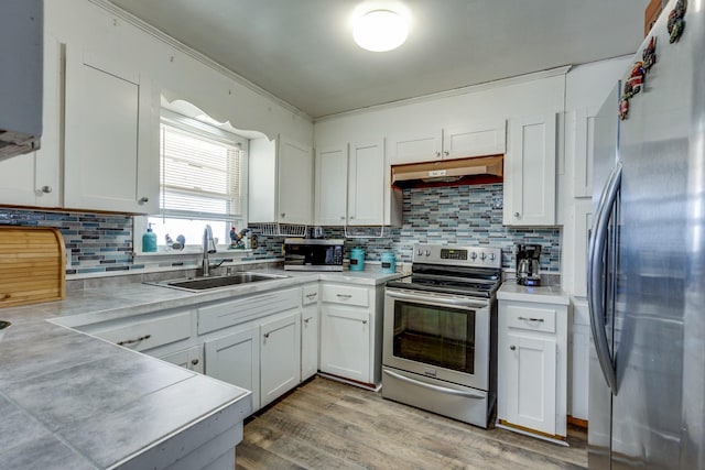 kitchen with light countertops, appliances with stainless steel finishes, white cabinets, a sink, and under cabinet range hood